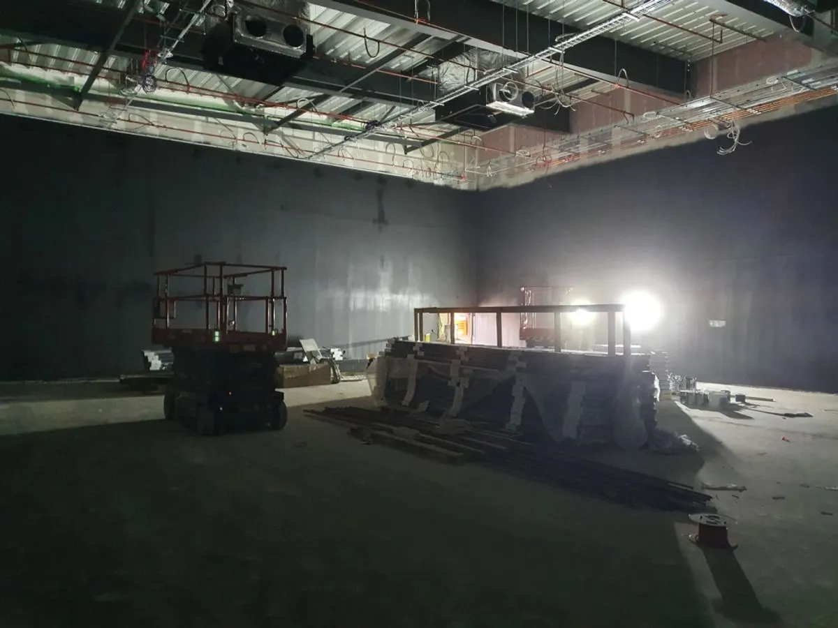 Commercial building interior with dark grey painted walls and scissor lift beside construction materials