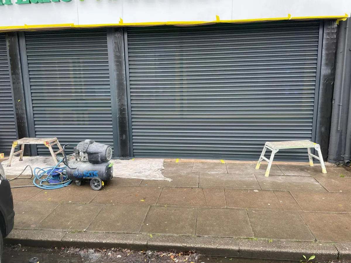 Row of shop shutters freshly sprayed dark grey with spray equipment on pavement outside