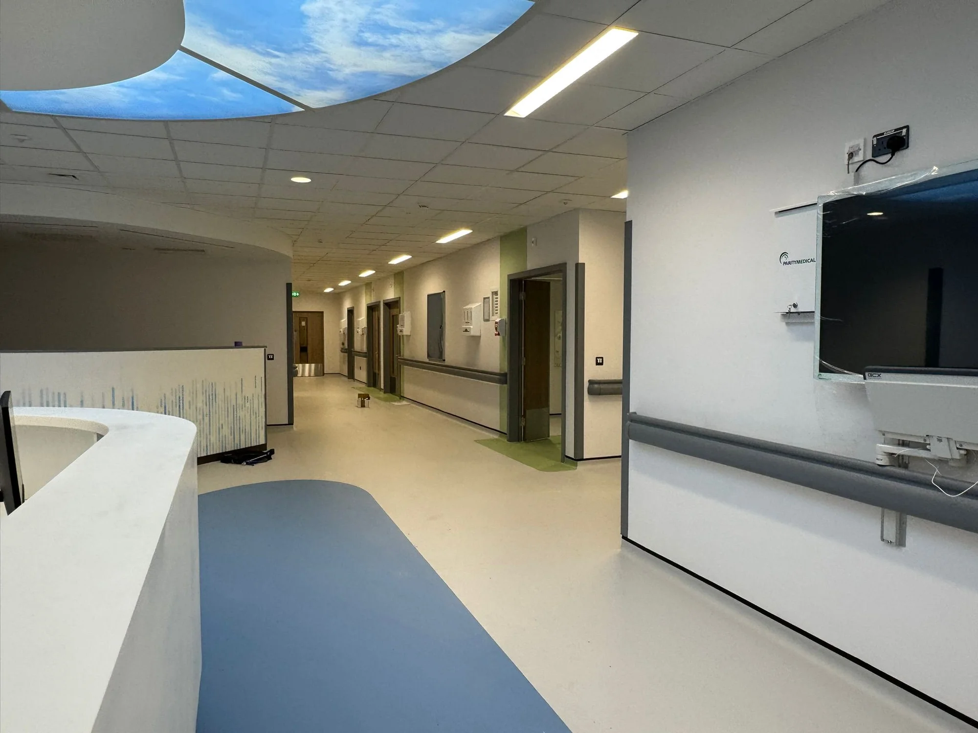 Freshly painted hospital corridor with sky ceiling feature blue accent flooring and nurses station