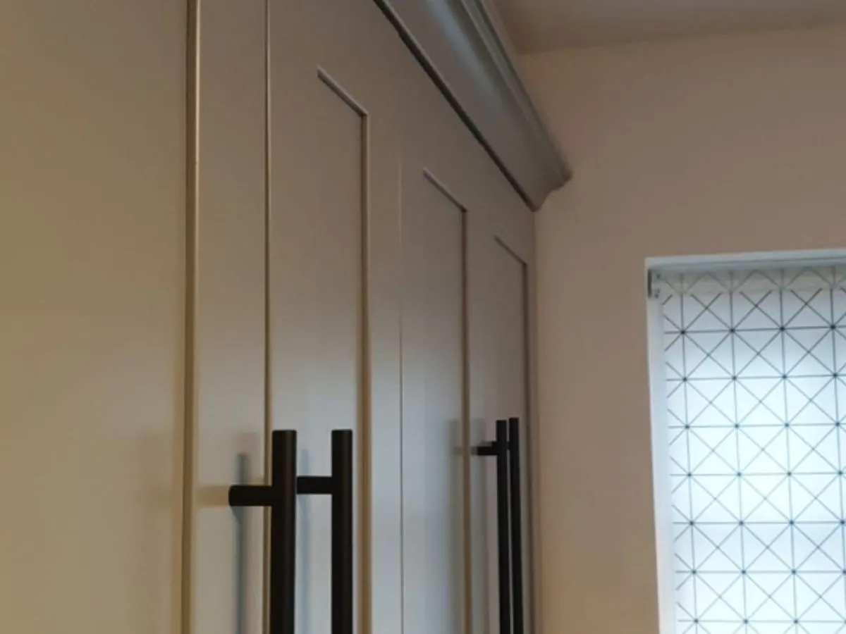 Close-up of tall cream sprayed kitchen larder cabinets with black bar handles