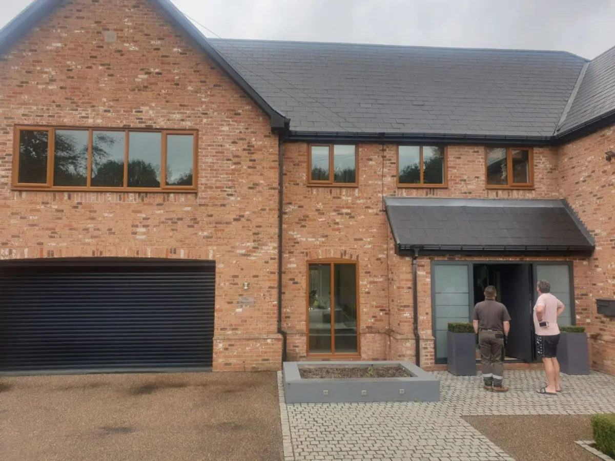 Large detached brick property with oak-effect sprayed UPVC windows and dark roller garage door