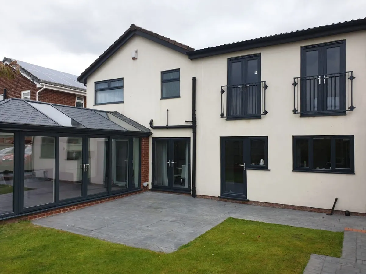 Rear of rendered house with dark grey sprayed UPVC windows conservatory doors and Juliet balconies